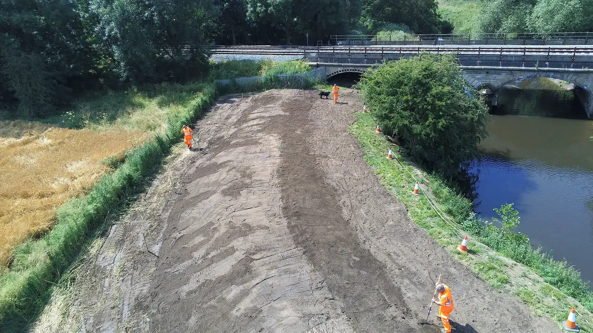 Site team preparing a works area beside a river and railway bridge