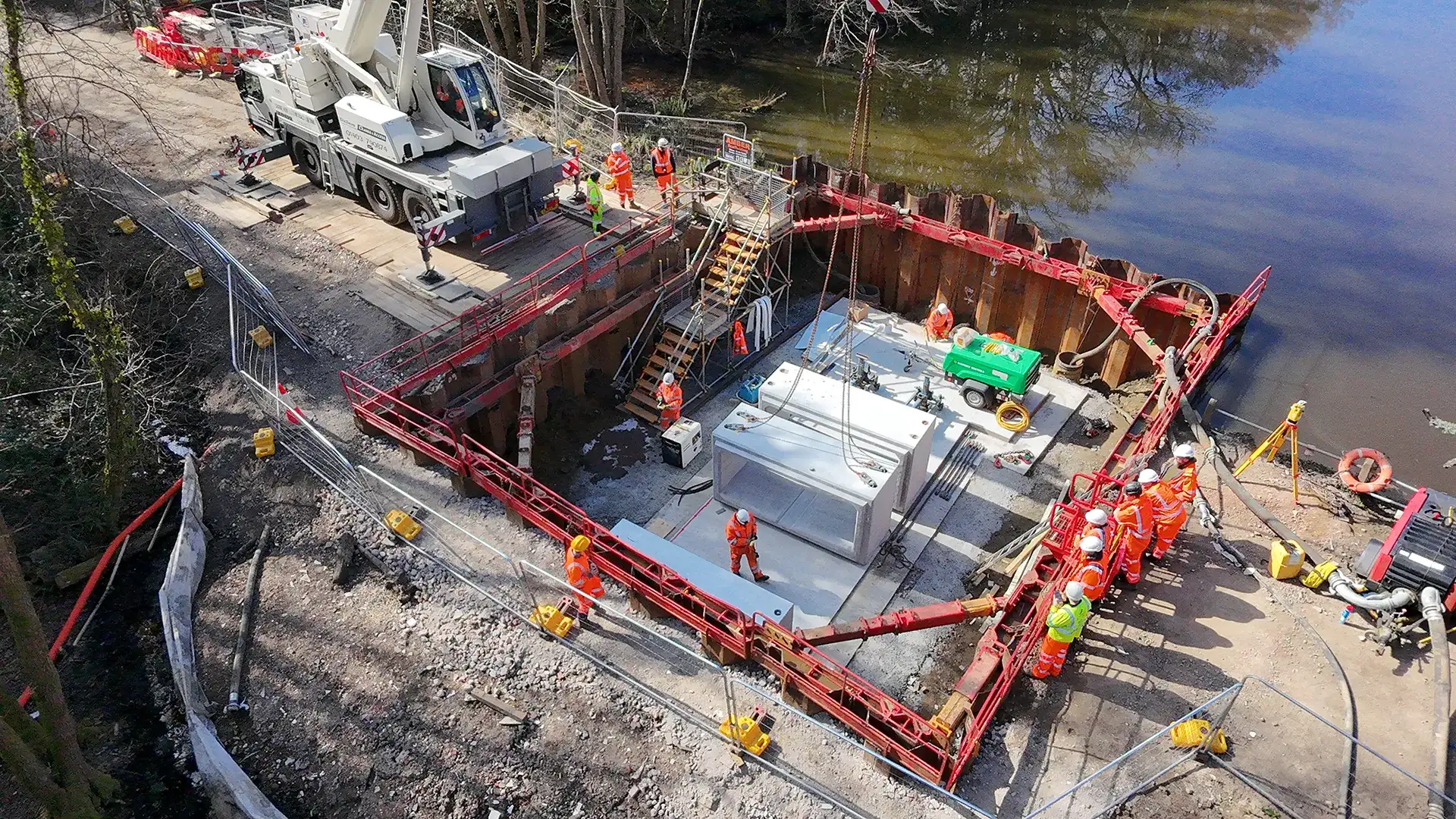 Construction team working within a temporary sheet-piled enclosure beside a river