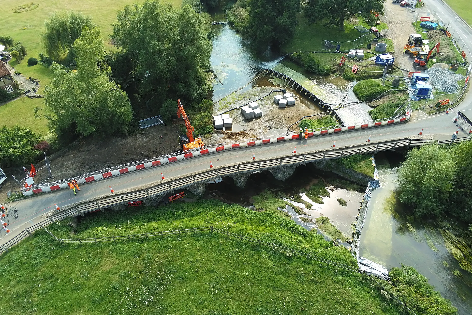 Aerial view of temporary water control works around a river bridge and weir in Tilford, Surrey
