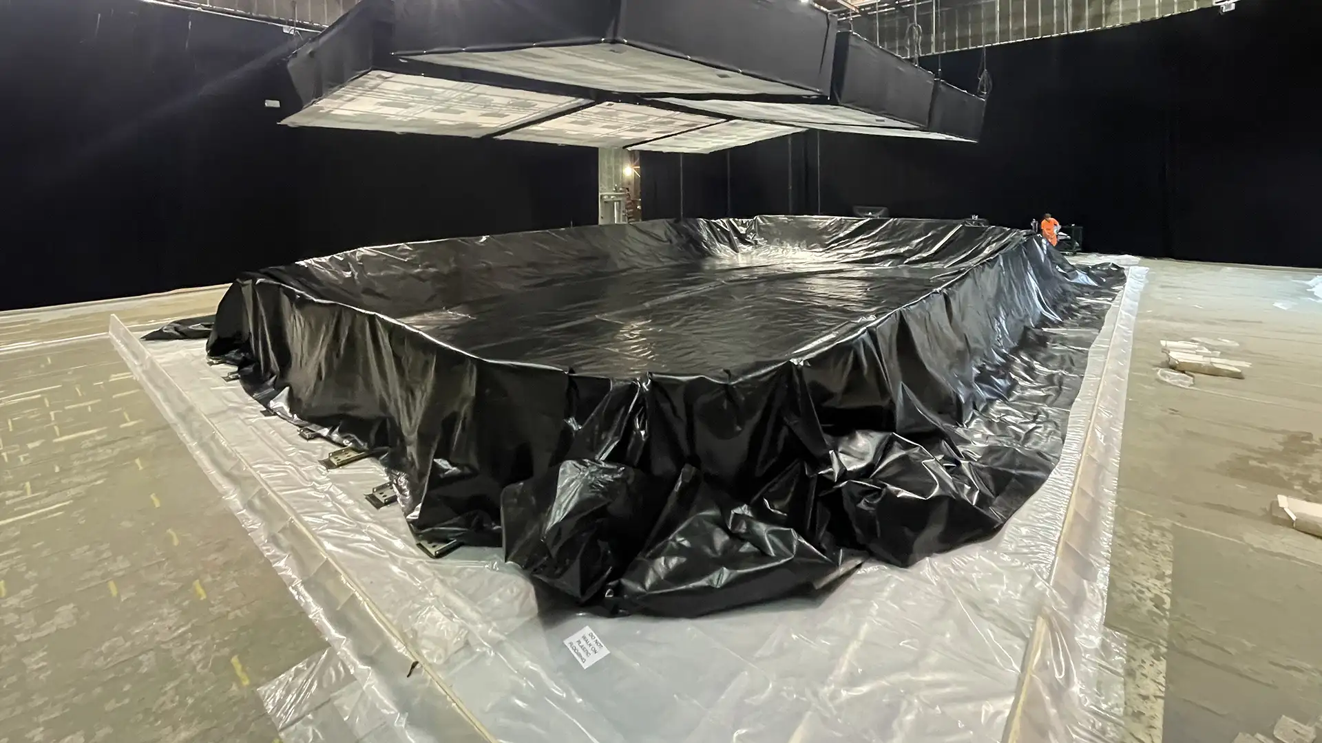 Large temporary water storage and containment basin under construction using a heavy-duty geomembrane liner within an indoor facility.