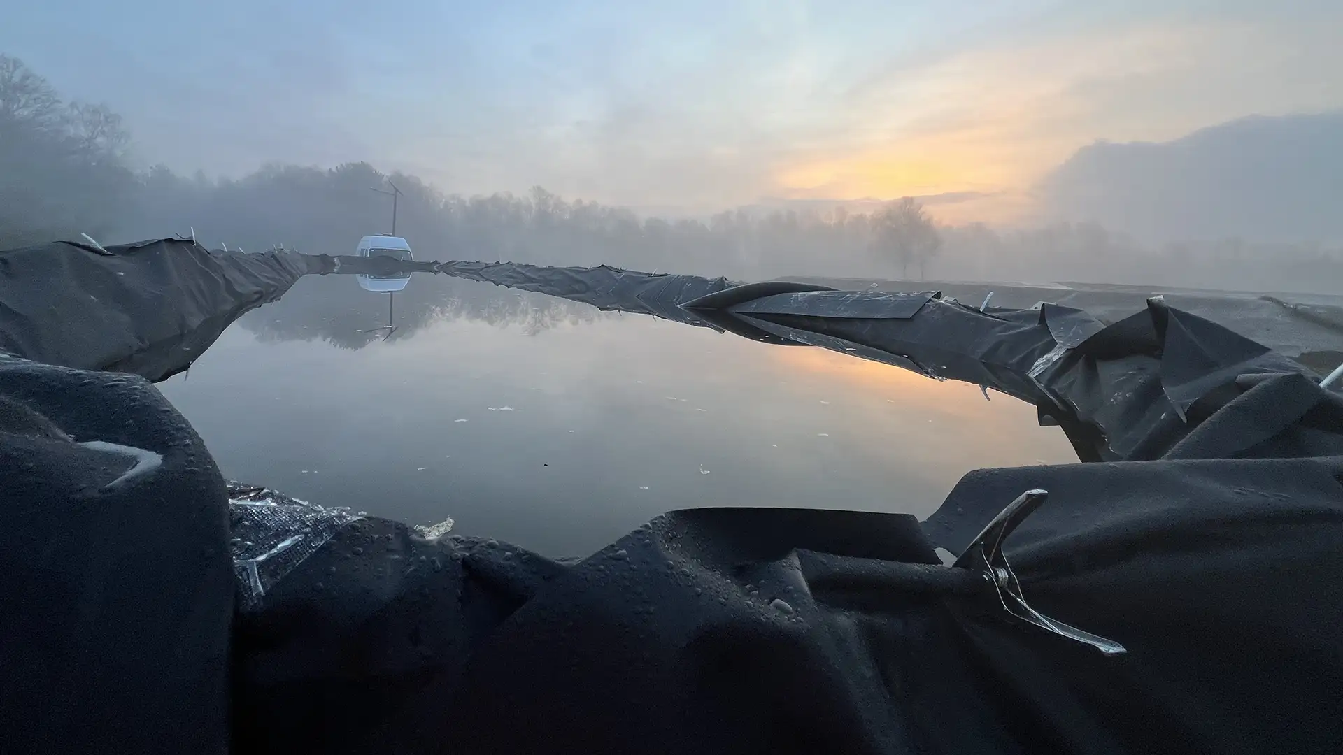 Large temporary water storage lagoon lined with an impermeable containment membrane during a water management project at sunrise.