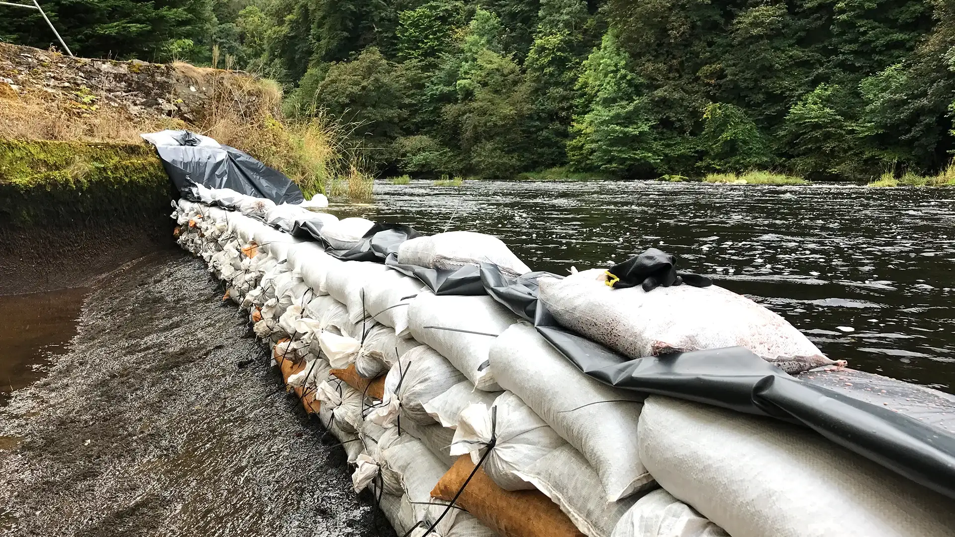 Temporary sandbag and membrane barrier installed to isolate a river and create a safe working area for engineering and maintenance works.